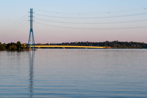 A modern high voltage electricity pylon standing on the shore during sunset. stock photo