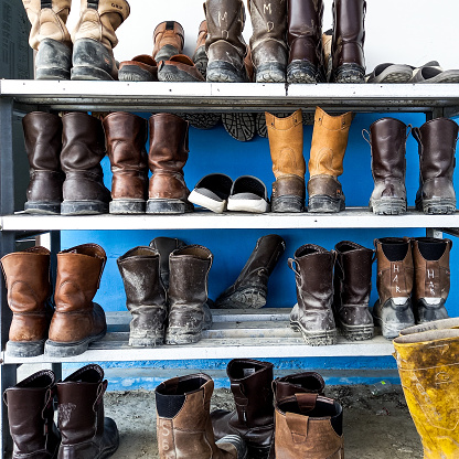 Rows of dirty safety shoes placed on a shoe rack outdoors