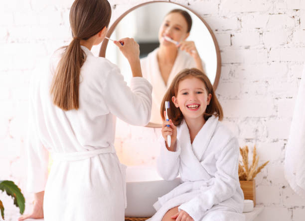 Mother and daughter brushing teeth together Happy young woman with little daughter in white bathrobes brushing teeth together in bathroom and enjoying morning time together teeth bonding stock pictures, royalty-free photos & images