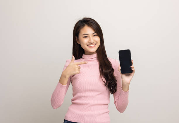 istock Pretty young asian woman using smartphone standing on isolated white background feeling happy. Shopping online payment with mobile phone. Excited and surprised female holding cellphone. 1332956290