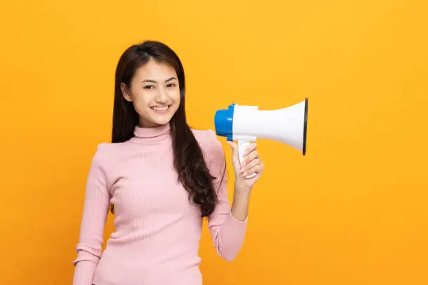 Photo of Shout out loud with megaphone. Young beautiful asian woman woman announces with a voice about promotions and advertisements for products at a discounted price. Shopping and fashion concept.