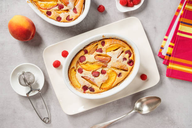 Traditional french pie clafoutis with fresh summer peaches and raspberry Traditional french pie clafoutis with fresh summer peaches and raspberry. Light- gray stone background, top view clafoutis stock pictures, royalty-free photos & images