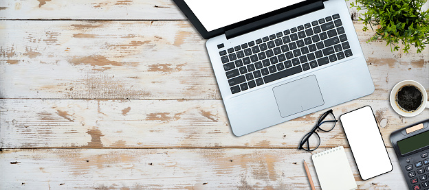 Wooden table top with plant pots, laptop, calculator, glasses, notebook on old wooden floor.