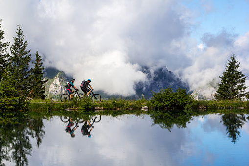 Brunni, Switzerland - August 06. 2021: People riding mountain bikes along the mountain lake Haerzlisee with reflection on the water surface. The area Haerzlisee above the Engelberg in Titlis region is a popular recreation place, which offers diverse outdoor activities, such as hiking, climbing, skiing.
