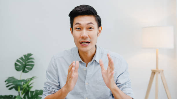 asia uomo d'affari distanziamento sociale in nuova situazione normale per la prevenzione dei virus guardando la presentazione della telecamera al collega sul piano in videochiamata mentre lavora in ufficio. - testa foto e immagini stock