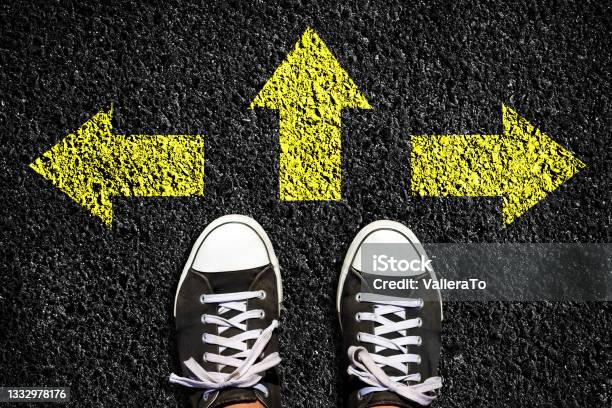 Sneakers On An Asphalt Road Yellow Arrows Pointing In Different Directions View From Above The Concept Of Choosing The Right Path Business Lifestyle Stock Photo - Download Image Now