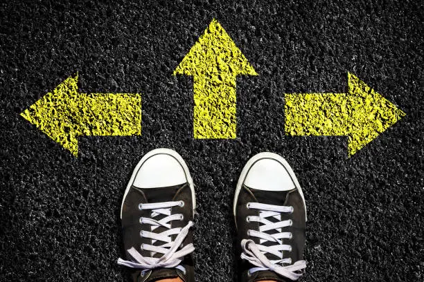 Photo of Sneakers on an asphalt road. Yellow arrows pointing in different directions. View from above. The concept of choosing the right path. Business. Lifestyle.