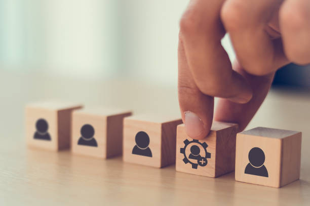 istock New skills concept to develop performance of human resources for business growth and digital transformation. Man holds wood cube with new skills icon symbol on many staff icon symbol; copy space. 1332980947
