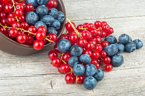 Delicious red currants and fresh blueberries in clay bowl on a wooden table. Mix of fresh berries.