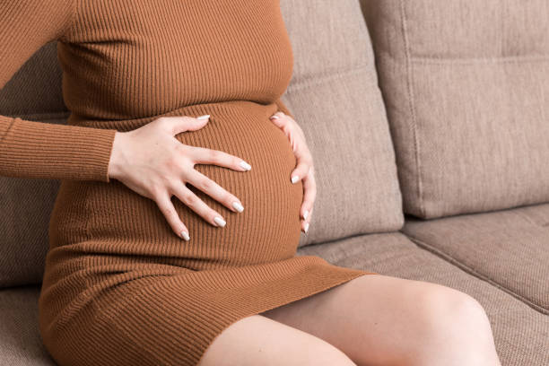 istock Pregnant Lady Having Massaging Lower belly Sitting On Sofa Indoor. Pregnancy Problems Concept. Maternity healthcare 1332983200