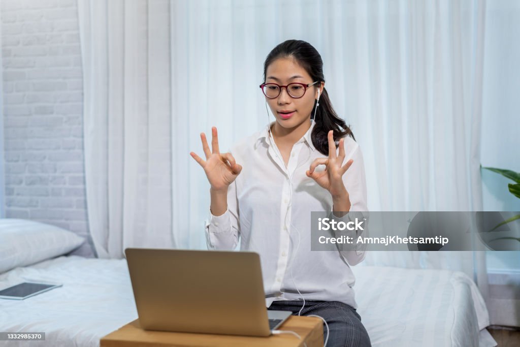 Young asian woman wears headphones to talk and video conferencing on a laptop computer in the bedroom at home. Sign Language Stock Photo