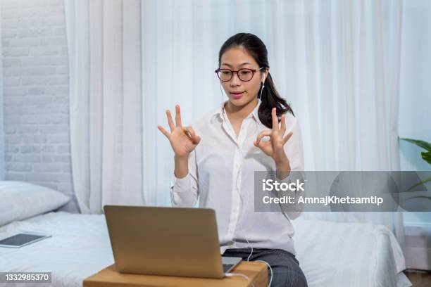 Young Asian Woman Wears Headphones To Talk And Video Conferencing On A Laptop Computer In The Bedroom At Home Stock Photo - Download Image Now
