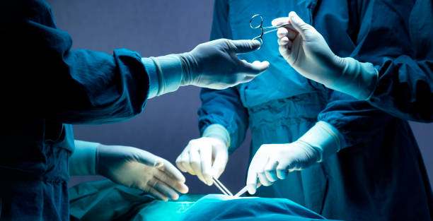 医師と看護師の医療チームは、病院の救急外来で外科手術を行っています。アシスタントは、手術中に外科医にハサミや器具を手渡します。 - 医療処置 ストックフォトと画像