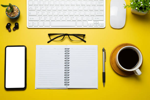 istock Top view of the working table modern equipment smartphone blank white screen placed on yellow background. Mock up 1332985504