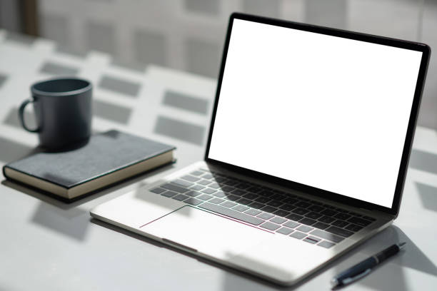istock Office desk with laptop blank white screen with notebook coffee mugs. Mock up. 1332985582