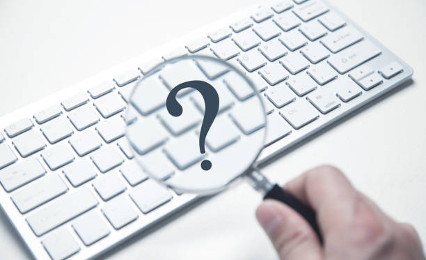 istock Male hand holds a magnifying glass and question mark on computer keyboard. 1332986017