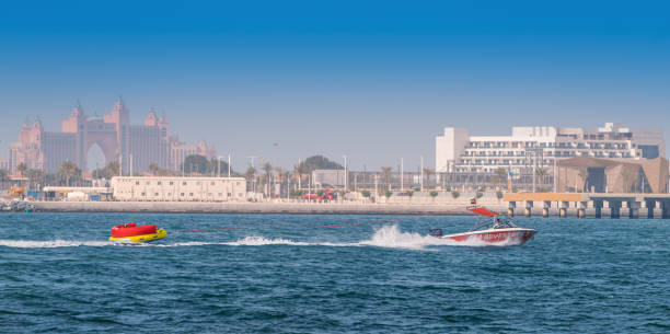 fans von extremsportarten und nervenkitzel fahren auf einem aufblasbaren donut, der von einem leistungsstarken motorboot vor der kulisse der palme jumeirah gezogen wird - the thrills stock-fotos und bilder