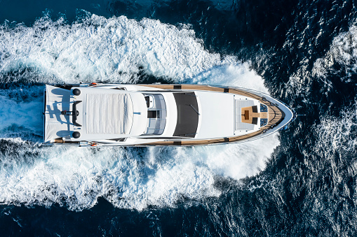 View from above, stunning aerial view of a luxury yacht cruising on a blue water with waves crashing on the bow of the boat. Costa Smeralda, Sardinia, Italy.