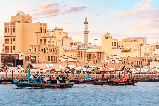 23 February 2021, Dubai, UAE: Abra Dhow wooden boats transport passengers from one bank of the Dubai Creek to the other with mosque minaret at the background