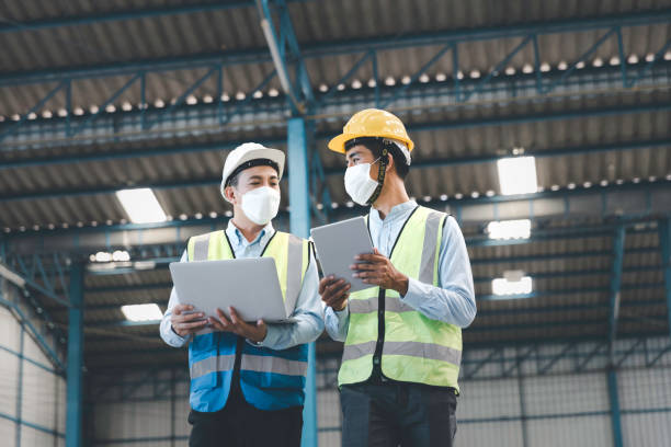 istock Factory manager and engineer in  medical mask and safety protective suite using computer laptop and digital tablet working discuss together 1332997082