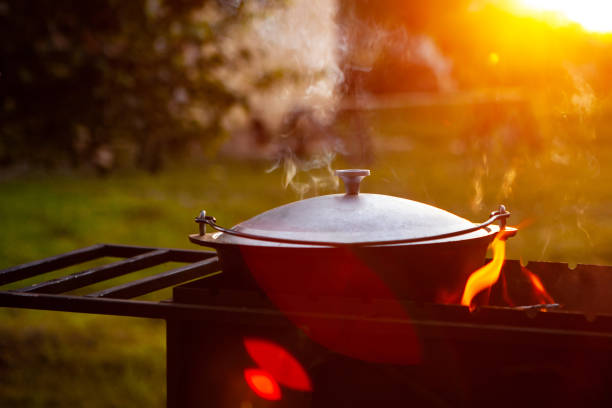 istock A saucepan, cauldron closed with a lid, in a grill on fire, from which steam comes out, on a natural background. Cooking in a pot on the fire. Camping concept. 1332999545