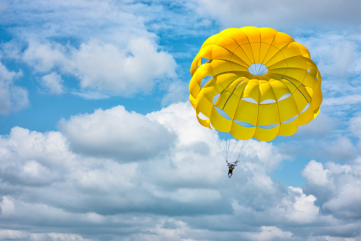 Paragliding using a yellow parachute on background of blue cloudy sky.