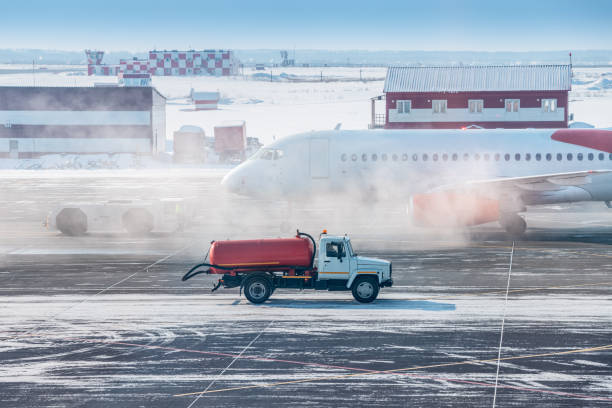 ein lkw mit treibstoff oder wasser fährt auf dem rollweg am flughafen vor dem hintergrund eines rauchenden flugzeugs im winter. konzept eines gefährlichen vorfalls und brand- oder motorausfalls - blizzard ice damaged snow stock-fotos und bilder