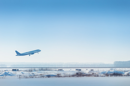 A passenger or cargo plane has left the runway and continues to climb in the air over a snow-covered winter airport