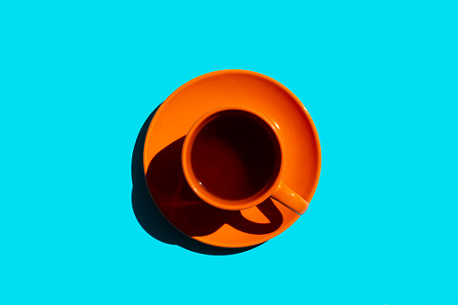 orange cup and saucer with black tea or coffee on the blue background. copy space. top view
