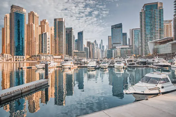 Photo of yacht and motor boats parking at the port near Dubai Marina Mall with row of high skyscrapers residential buildings and hotels