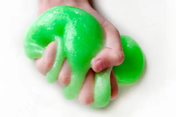 Photo of Hand Playing with textured slime with bubbles, stretching the gooey substance. Female teen hand holding green shining slime, squeezing it. Adorable Girl stretching slime toy to the sides. Liquid toy.