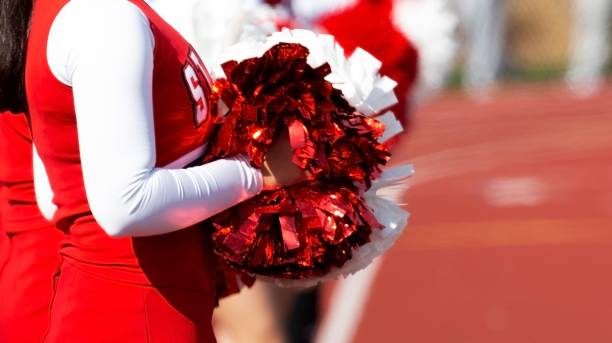 Side view of cheerleaders red and white pompoms High school cheerleaders standing on a red track holding their pompoms in front of them. cheerleader photos stock pictures, royalty-free photos & images