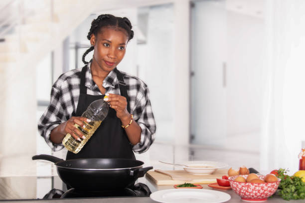 femme afro-américaine tenant une bouteille d’huile derrière une poêle à frire - black olive photos et images de collection