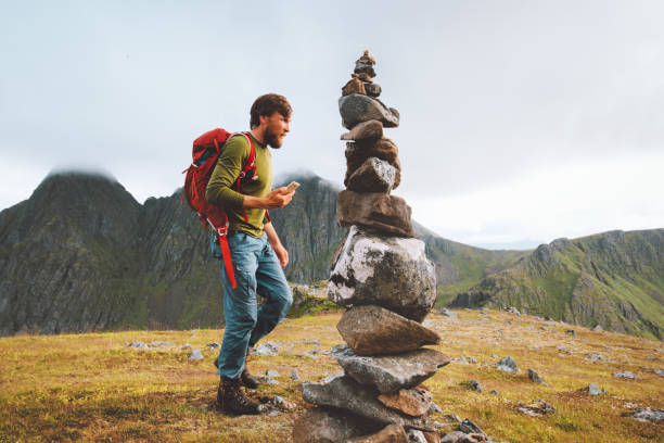Man hiking with backpack using smartphone for navigation rock cairn marking route on mountain summit Travel healthy lifestyle concept active adventure vacations