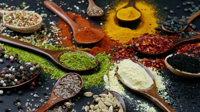 Dry colorful spices in spoons and bowls with fresh seasoning on dark background, top view