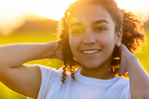 Beautiful biracial mixed race African American teenager teen girl young woman smiling outside backlit at sunset or sunrise