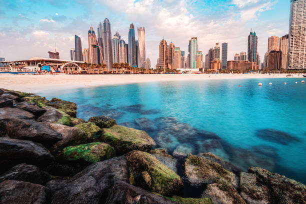 majestätische felsen brechen im vordergrund mit dem azurblauen wasser des persischen golfs und bunten wolkenkratzern in der marina und jbr bay area in dubai - dubai beach hotel skyline stock-fotos und bilder