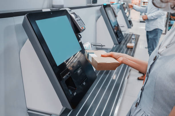 une femme scanne le code-barres de sa boîte à lunch pour le paiement sans espèces à la caisse en libre-service du supermarché. de telles machines kiosques permettent d’augmenter le débit et de réduire la file d’attente dans le magasin - libre service photos et images de collection