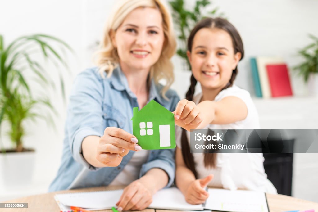 people, charity, family and home concept - close up of woman and girl holding green paper house cutout in cupped hands people, charity, family and home concept - close up of woman and girl holding green paper house cutout in cupped hands. Homeschooling Stock Photo