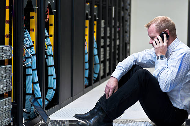 businessman with laptop and a smartphone in network server room stock photo