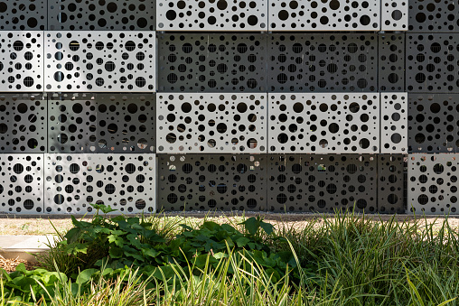 Sheet metal facade with patterns of circles. in the front there is a sidewalk and a landscaped area.
