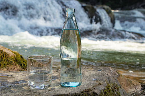 Natural drinking water in a bottle and glass beaker on nature background river.