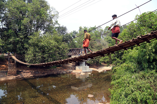 It is a footbridge near Aralam Farm, an important tribal rehabilitation area in Kannur district, Kerala state, India.\nThe villagers pass through this bridge, which is full of dangers, literally holding on to life.\nPedestrians living inside the Aralam Farm walking across the bridge, which can be dangerous at any time.