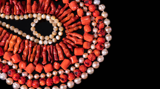 le corail rouge brillant et les colliers de perles blanches irisées sont disposés en cercles sur un fond noir. plat lay. - black pearl pearl horizontal necklace photos et images de collection