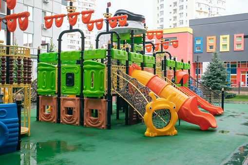 A courtyard of high-rise buildings with a new modern colorful and large playground on a rainy summer day without people. Empty outdoor playground. A place for children's games and sports