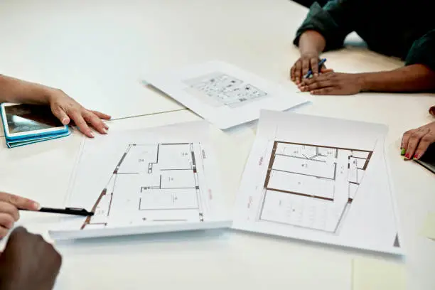 Close-up of men and women sitting at conference table discussing multi-story floor plans for property they are marketing.