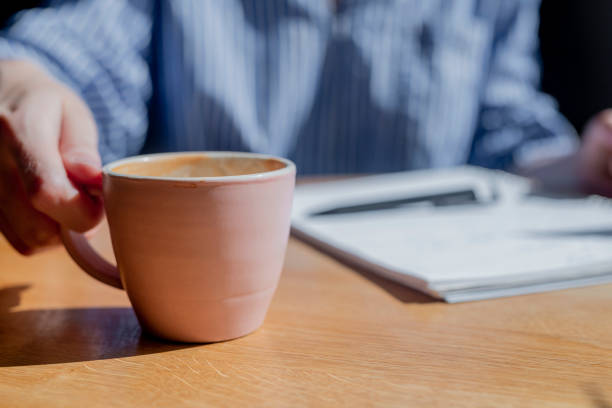 istock Female hand closeup taking coffee cup in cafe with blurred notebook and pen on background 1333064348