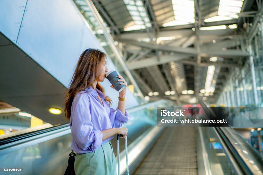 Asian woman is taking the escalator to get a taxi. Asian business woman, wanting to call a taxi to go home, hurried up the escalator to reach a public bus stop. Coffee - Drink Stock Photo