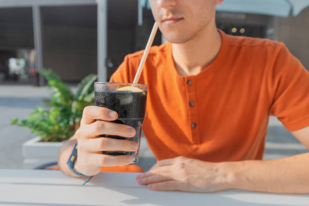 Man drinks unusual sparkling water in black color with ice and lemon with a drinking straw Man drinks unusual sparkling water in black color with ice and lemon with a drinking straw coke coal stock pictures, royalty-free photos & images