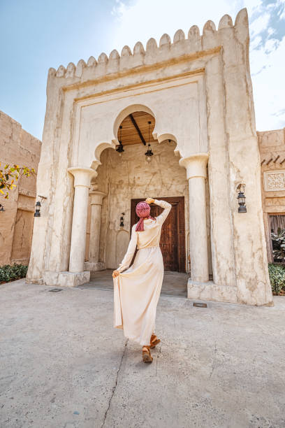 femme touriste portant turban rouge et biege longue robe se promène dans les vieilles rues étroites de bur dubai et creek. concept de voyage et de tourisme - cocklebur photos et images de collection